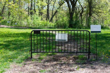 Metal barrier with path closed sign blocking a walking trail in a green park during maintenance and restoration works.