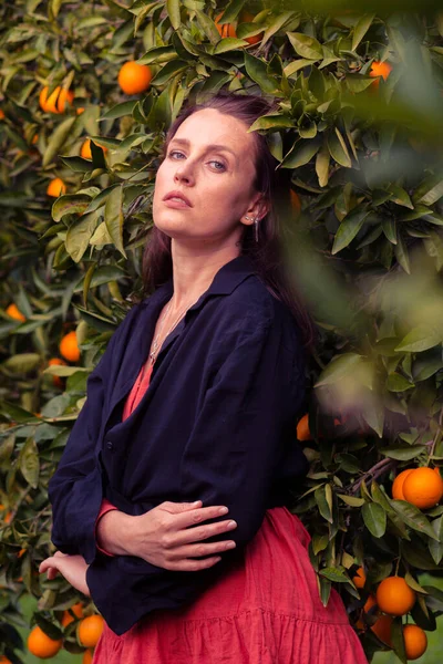 Beautiful Girl in the Orange Garden and ripe oranges on the branches of trees. Photo of a girl in the garden among fruit trees.