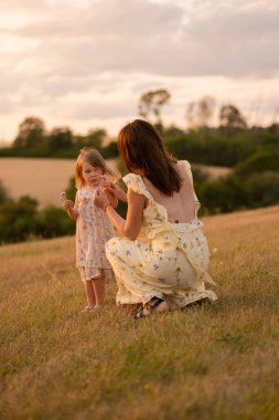 Gün batımında küçük kızını tarlada tutan güzel bir bayan. Güzel sarı elbiseli çocuklu bir kadın gün batımında tarlada poz verir..