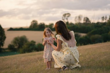 Gün batımında küçük kızını tarlada tutan güzel bir bayan. Güzel sarı elbiseli çocuklu bir kadın gün batımında tarlada poz verir..