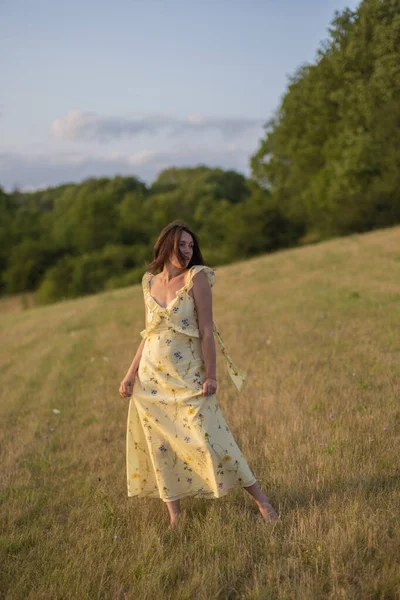 Genç ve güzel bir bayan gün batımında çıplak ayakla bir tarlada yürüyor. Güzel sarı elbiseli bir kız gün batımında tarlada poz verir..