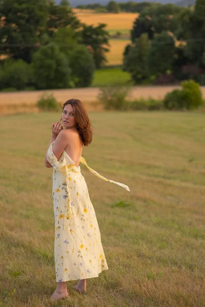 Genç ve güzel bir bayan gün batımında çıplak ayakla bir tarlada yürüyor. Güzel sarı elbiseli bir kız gün batımında tarlada poz verir..
