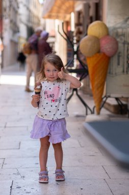 Hırvatistan 'ın antik bir şehrinin caddesinde dondurmalı güzel beyaz kız. Yoldan geçenler arasında bir kız dondurmanın tadını çıkarıyor..