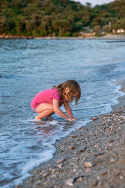 Küçük kız kumlu sahilde oynuyor. Pembe tişörtlü ve güzel bir deniz sahilinde mayo giyen bir kız. Adriyatik Denizi 'nin en temiz suları.