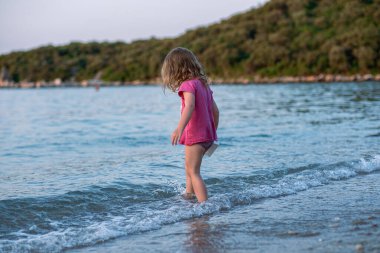 Küçük kız kumlu sahilde oynuyor. Pembe tişörtlü ve güzel bir deniz sahilinde mayo giyen bir kız. Adriyatik Denizi 'nin en temiz suları.