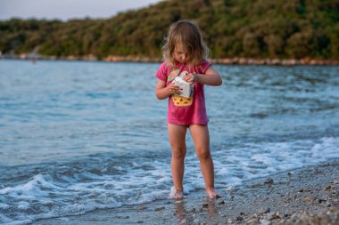 Küçük kız kumlu sahilde oynuyor. Pembe tişörtlü ve güzel bir deniz sahilinde mayo giyen bir kız. Adriyatik Denizi 'nin en temiz suları.