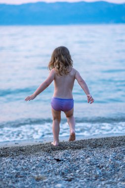 Küçük kız kumlu sahilde oynuyor. Güzel bir deniz sahilinde pembe şortlu bir kız. Adriyatik Denizi 'nin en temiz suları.