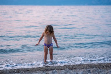 Küçük kız kumlu sahilde oynuyor. Güzel bir deniz sahilinde pembe şortlu bir kız. Adriyatik Denizi 'nin en temiz suları.