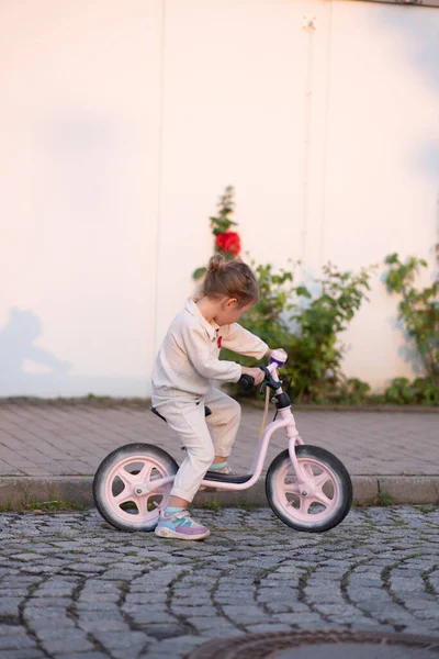 ピンクのスーツの小さな女の子は 夕日の光の中でピンクのバランスバイクに乗っています 子供の自転車について — ストック写真