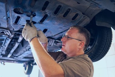 Gözlüklü Adam Garajda Araba Bakımı Yapıyor. Araba tamirhanesinde deneyimli bir uzman tarafından araba tamiri. Arabadaki yağ ve filtreyi değiştiriyorum. Bir oto tamircisi araba tamiratı yapar..