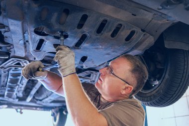 Gözlüklü Adam Garajda Araba Bakımı Yapıyor. Araba tamirhanesinde deneyimli bir uzman tarafından araba tamiri. Arabadaki yağ ve filtreyi değiştiriyorum. Bir oto tamircisi araba tamiratı yapar..
