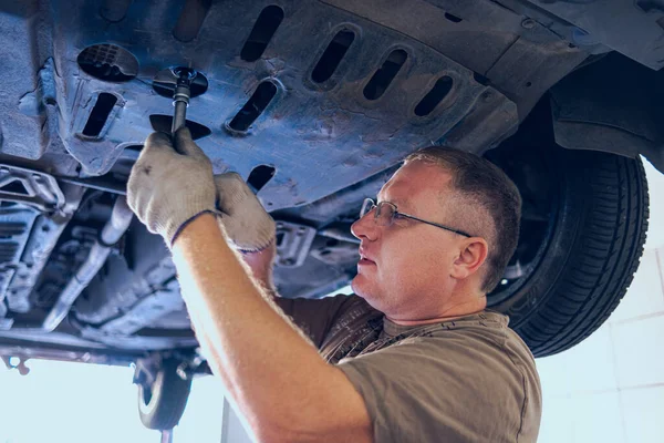 Gözlüklü Adam Garajda Araba Bakımı Yapıyor. Araba tamirhanesinde deneyimli bir uzman tarafından araba tamiri. Arabadaki yağ ve filtreyi değiştiriyorum. Bir oto tamircisi araba tamiratı yapar..