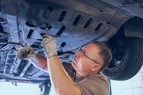 Gözlüklü Adam Garajda Araba Bakımı Yapıyor. Araba tamirhanesinde deneyimli bir uzman tarafından araba tamiri. Arabadaki yağ ve filtreyi değiştiriyorum. Bir oto tamircisi araba tamiratı yapar..