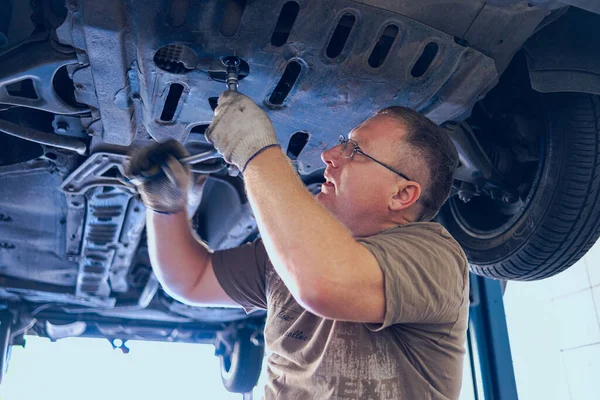 Gözlüklü Adam Garajda Araba Bakımı Yapıyor. Araba tamirhanesinde deneyimli bir uzman tarafından araba tamiri. Arabadaki yağ ve filtreyi değiştiriyorum. Bir oto tamircisi araba tamiratı yapar..