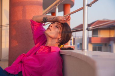 Balkonda denize bakan güzel bir kız. Kırmızı gömlekli ve mavi kotlu bir kız üst kattaki dairesinin balkonunda dinleniyor..