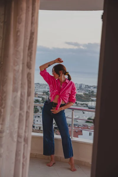 Beautiful girl on the balcony overlooking the sea. A girl in a red shirt and blue jeans rests on the balcony of her apartment on a high floor.