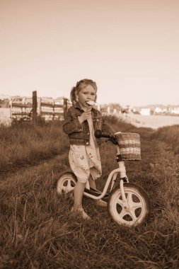 Avrupalı görünümlü küçük güzel kız pembe bisikletinin üzerinde otururken dondurma yiyor. Güneşli bir günde bisiklet süren bir kız.