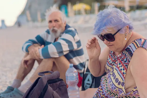 Büyükbabam ve büyükannem deniz kenarında oturuyorlar. Bir çift renkli yaşlı insan plajda dinleniyor. Yaşlı turistler hayattan zevk alıyor