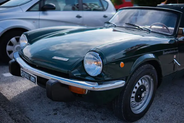 stock image Ancona, Italy - 16 Sep 2023: An old vintage perfectly restored Triumph car is parked on the street on a sunny summer day. Green old Triumph roadster on a flowery street.