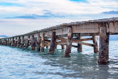Denize uzanan ahşap bir iskelenin fotoğrafı. İskelenin yan manzarası güzelmiş. Sakin turkuaz deniz suyu, ahşap köprü yapısı ve güzel gökyüzü..