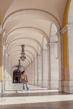 Bir kız, kolonlarla antik bir binanın koridorunda yürüyor. Kaliteli lambaları olan güzel bir sütundaki genç bir kız..