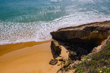 Titreyen okyanusun üzerinden güzel bir manzara. Sarı kumlu kumsal ve mağara oluşturan bir kaya. Prainha das Pocas
