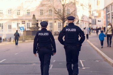 İki Alman polis memuru şehir caddesi boyunca yürüyorlar. Polis üniformalı bir adam ve kadın. Arkasından bakılan Almanca 