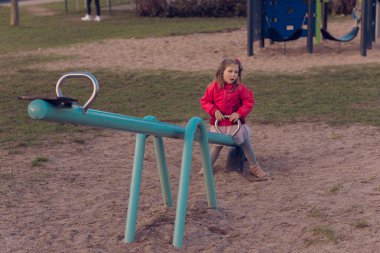 Güzel küçük bir kız parkta tek başına oynuyor. Kız tek başına sıkılmış ve tahterevallide ya da tahterevalliye binecek kimsesi yok ve salıncağın bir tarafında oturuyor..