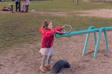 Güzel küçük bir kız parkta tek başına oynuyor. Kız tek başına sıkılmış ve tahterevallide ya da tahterevalliye binecek kimsesi yok ve salıncağın bir tarafında oturuyor..