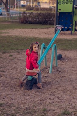 Güzel küçük bir kız parkta tek başına oynuyor. Kız tek başına sıkılmış ve tahterevallide ya da tahterevalliye binecek kimsesi yok ve salıncağın bir tarafında oturuyor..