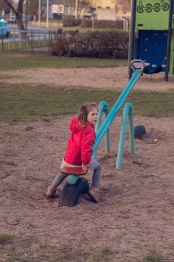 Güzel küçük bir kız parkta tek başına oynuyor. Kız tek başına sıkılmış ve tahterevallide ya da tahterevalliye binecek kimsesi yok ve salıncağın bir tarafında oturuyor..