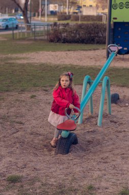 Güzel küçük bir kız parkta tek başına oynuyor. Kız tek başına sıkılmış ve tahterevallide ya da tahterevalliye binecek kimsesi yok ve salıncağın bir tarafında oturuyor..