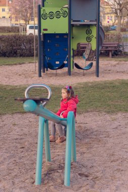 Güzel küçük bir kız parkta tek başına oynuyor. Kız tek başına sıkılmış ve tahterevallide ya da tahterevalliye binecek kimsesi yok ve salıncağın bir tarafında oturuyor..