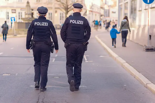 İki Alman polis memuru şehir caddesi boyunca yürüyorlar. Polis üniformalı bir adam ve kadın. Arkasından bakılan Almanca 