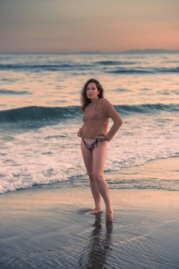 Sıcak bir yaz akşamında sahilin arka planında poz veren güzel bir kız. Arka planda güzel bokeh ve deniz dalgaları.