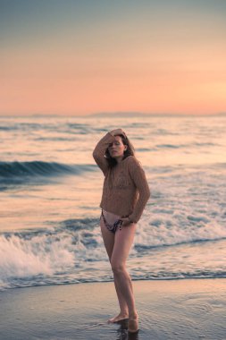 Sıcak bir yaz akşamında sahilin arka planında poz veren güzel bir kız. Arka planda güzel bokeh ve deniz dalgaları.