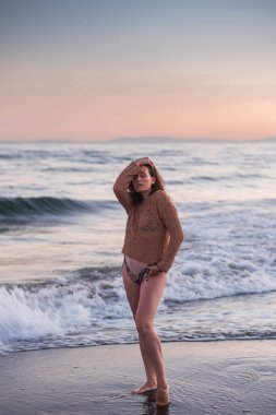 Sıcak bir yaz akşamında sahilin arka planında poz veren güzel bir kız. Arka planda güzel bokeh ve deniz dalgaları.