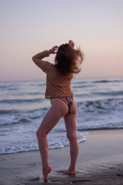 Sıcak bir yaz akşamında sahilin arka planında poz veren güzel bir kız. Arka planda güzel bokeh ve deniz dalgaları.