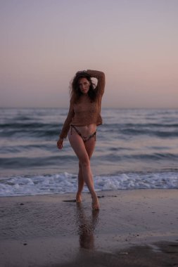 Sıcak bir yaz akşamında sahilin arka planında poz veren güzel bir kız. Arka planda güzel bokeh ve deniz dalgaları.