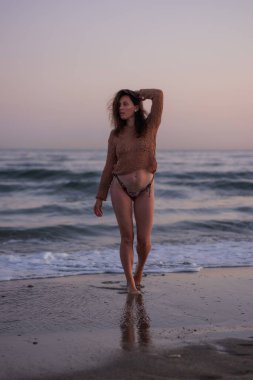 Sıcak bir yaz akşamında sahilin arka planında poz veren güzel bir kız. Arka planda güzel bokeh ve deniz dalgaları.