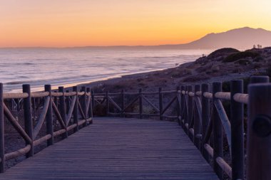 Denize açılan korkuluklu ahşap platform. Tahta levhalarla döşenmiş yol denize iniyor. Arka plandaki açık gökyüzünde günbatımının güzel gradyanı.