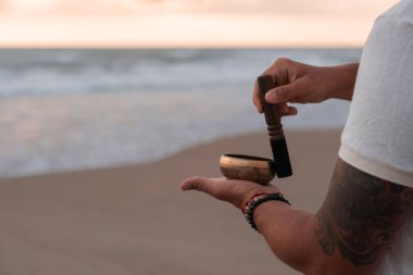 Beyaz yaz kıyafetleri içinde genç yakışıklı adam yaz akşamları sahilde şarkı söyler. Adam yoga yapıyor ve şarkı söyleyen kâse ve deniz dalgalarından gelen sesle meditasyon yapıyor. 4K video.