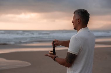 Beyaz yaz kıyafetleri içinde genç yakışıklı adam yaz akşamları sahilde şarkı söyler. Adam yoga yapıyor ve şarkı söyleyen kâse ve deniz dalgalarından gelen sesle meditasyon yapıyor. 4K video.