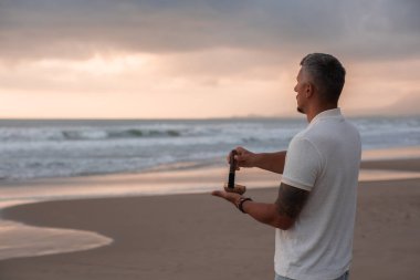 Beyaz yaz kıyafetleri içinde genç yakışıklı adam yaz akşamları sahilde şarkı söyler. Adam yoga yapıyor ve şarkı söyleyen kâse ve deniz dalgalarından gelen sesle meditasyon yapıyor. 4K video.