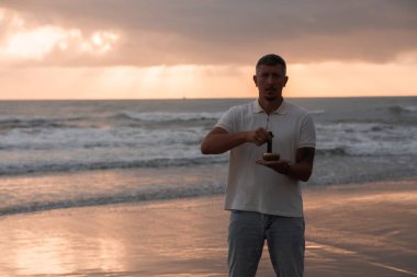 Beyaz yaz kıyafetleri içinde genç yakışıklı adam yaz akşamları sahilde şarkı söyler. Adam yoga yapıyor ve şarkı söyleyen kâse ve deniz dalgalarından gelen sesle meditasyon yapıyor. 4K video.