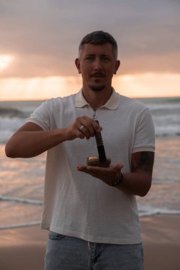 Beyaz yaz kıyafetleri içinde genç yakışıklı adam yaz akşamları sahilde şarkı söyler. Adam yoga yapıyor ve şarkı söyleyen kâse ve deniz dalgalarından gelen sesle meditasyon yapıyor. 4K video.