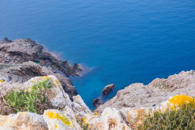 Yüksek kayalıklar denizin derinliklerine doğru uzanıyor. Güzel deniz manzarası. Sakin mavi deniz ve berrak gökyüzü büyük uçurumların üzerinde.