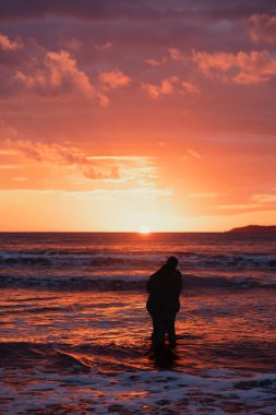 Denizde renkli bir gün batımı. Deniz sahilinde gün batımı. Çıplak adam ve kadın sarılıyor, denizde duruyor. Birbirine aşık bir çift gün batımının arka planına karşı denizde duruyor..