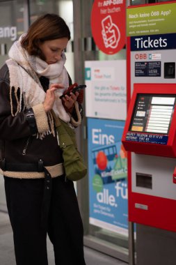 Innsbruk, Avusturya - 03.12.2024: Anne ve oğlu istasyondaki bir makineden tren bileti alıyorlar. Trenle seyahat, yenilikler, bilet satış teknolojileri..