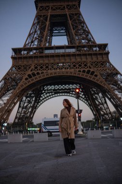 Paris 'teki Eyfel Kulesi' nin arka planında poz veren güzel bir kız. Paris 'te akşam, parıldayan Eyfel Kulesi ve güzel genç bir kadın..